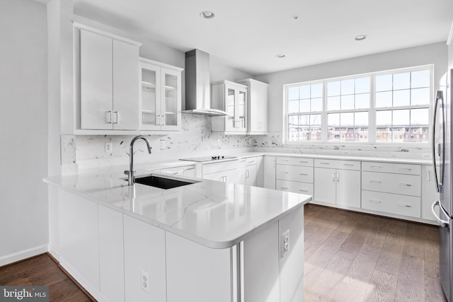 kitchen with wall chimney range hood, dark hardwood / wood-style floors, kitchen peninsula, sink, and white cabinets