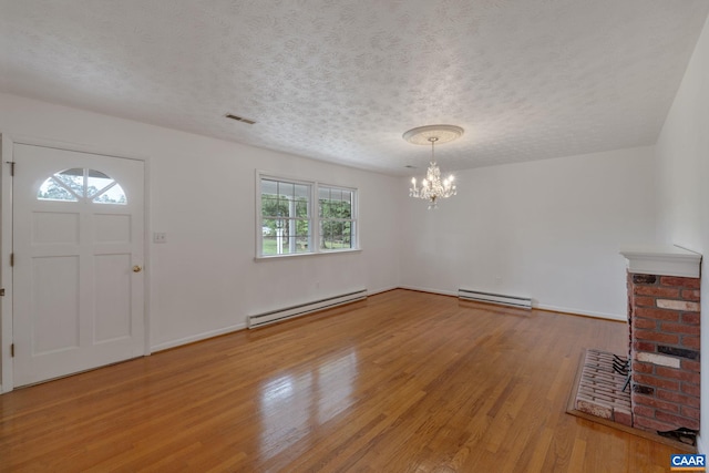 entrance foyer featuring a textured ceiling, a brick fireplace, baseboard heating, and hardwood / wood-style floors