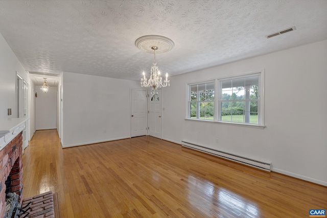 spare room with a baseboard heating unit, a notable chandelier, a brick fireplace, light wood-type flooring, and a textured ceiling