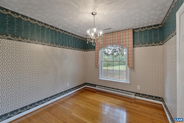 unfurnished dining area with an inviting chandelier, a baseboard heating unit, a textured ceiling, and wood-type flooring