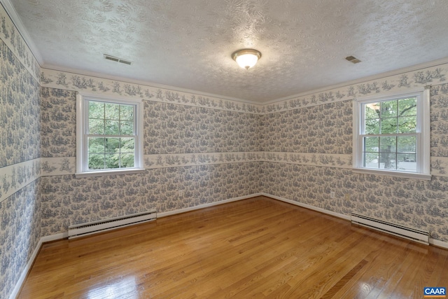 empty room featuring a healthy amount of sunlight, hardwood / wood-style flooring, and a baseboard heating unit