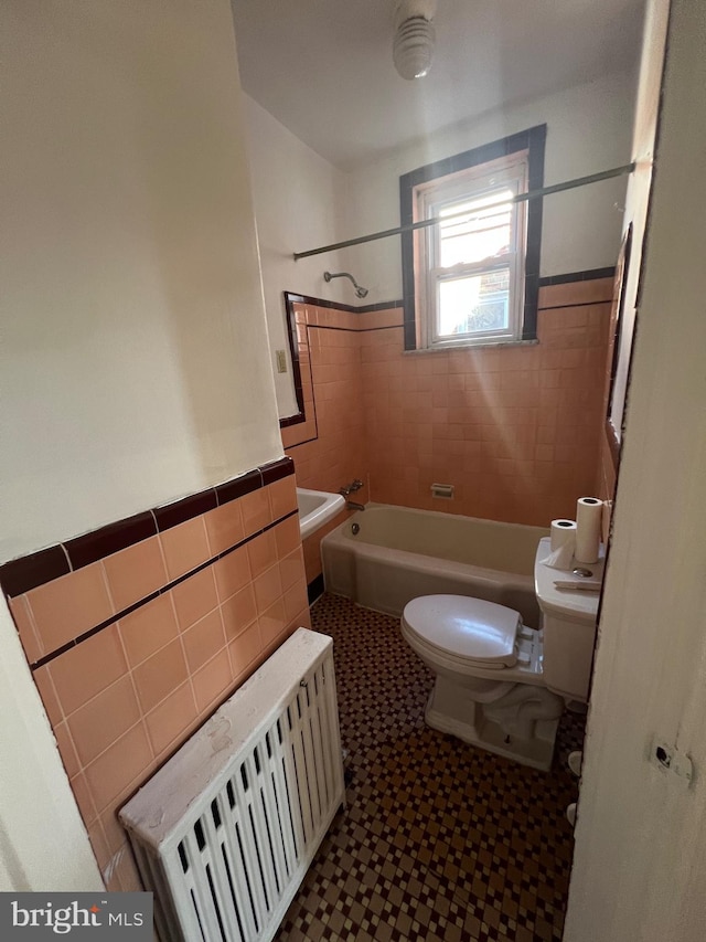 bathroom with toilet, tiled shower / bath combo, tile walls, and radiator heating unit