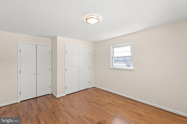 unfurnished bedroom featuring multiple closets and light wood-type flooring