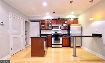 kitchen featuring appliances with stainless steel finishes, crown molding, hanging light fixtures, and light wood-type flooring