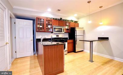 kitchen with ornamental molding, light hardwood / wood-style flooring, decorative light fixtures, and stainless steel appliances