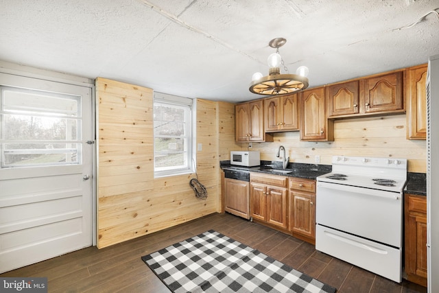 kitchen featuring dark hardwood / wood-style floors, wooden walls, sink, a chandelier, and white appliances