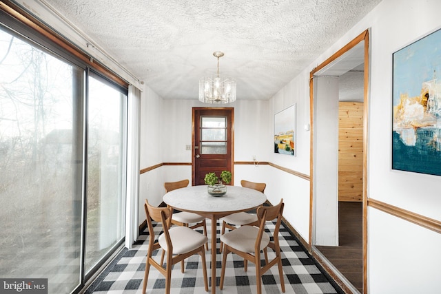 dining space with dark wood-type flooring, a textured ceiling, and a chandelier