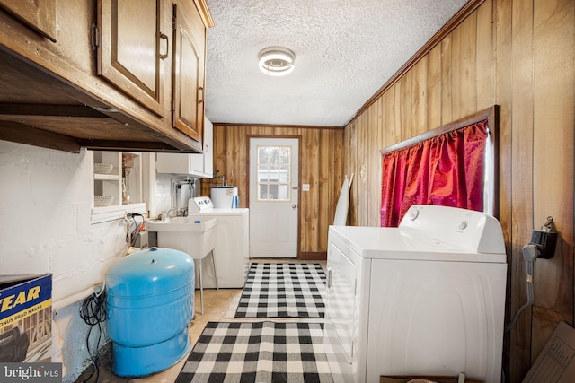 clothes washing area featuring wood walls, washing machine and dryer, cabinet space, a textured ceiling, and electric water heater
