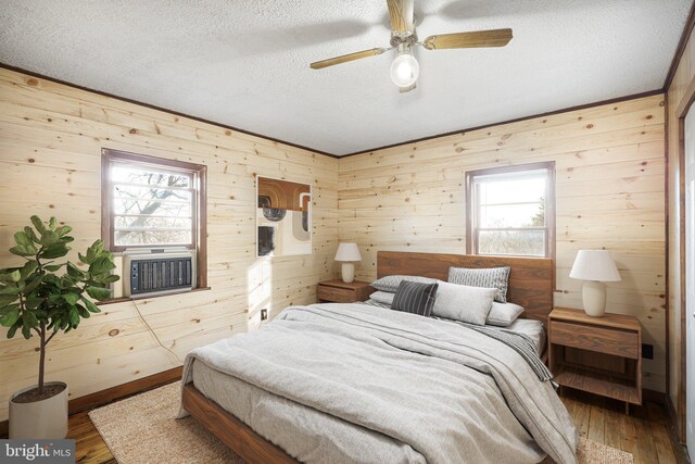 bedroom featuring ceiling fan, wood walls, multiple windows, and hardwood / wood-style floors