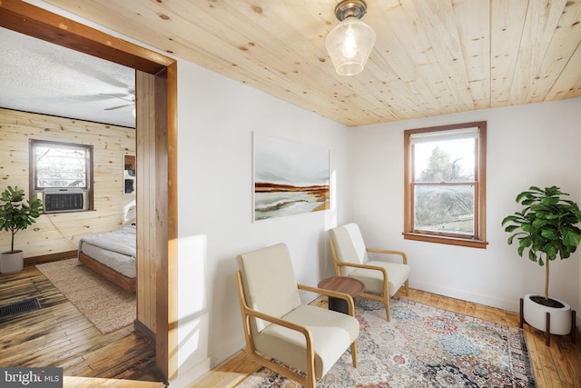 living area with ceiling fan, wood walls, cooling unit, and hardwood / wood-style floors