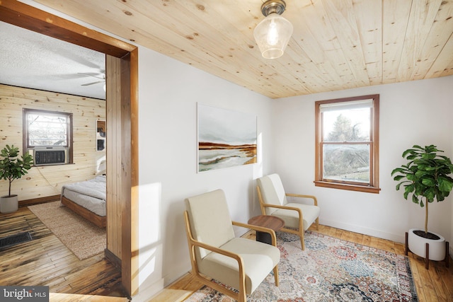 sitting room with wood-type flooring, baseboards, cooling unit, and wooden walls