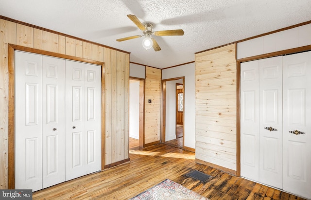 unfurnished bedroom with ceiling fan, wood walls, multiple closets, and light hardwood / wood-style flooring