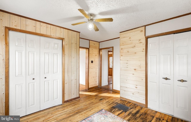 unfurnished bedroom featuring wooden walls, visible vents, ornamental molding, light wood-style floors, and baseboards