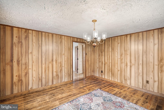 empty room featuring a notable chandelier, a textured ceiling, wooden walls, and wood-type flooring