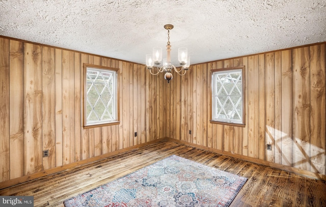 empty room with an inviting chandelier, hardwood / wood-style floors, wooden walls, and a textured ceiling