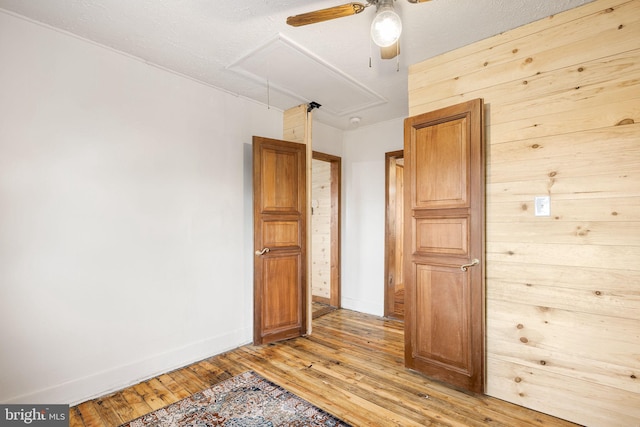 unfurnished bedroom with ceiling fan, light hardwood / wood-style flooring, and wooden walls