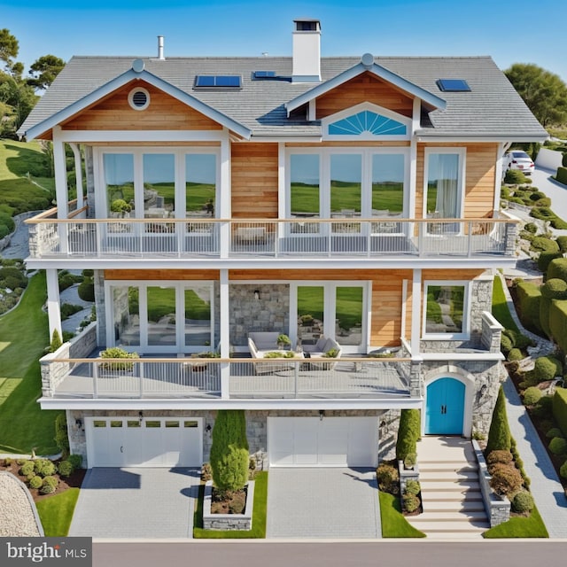 back of house with stone siding, a chimney, a balcony, an attached garage, and french doors