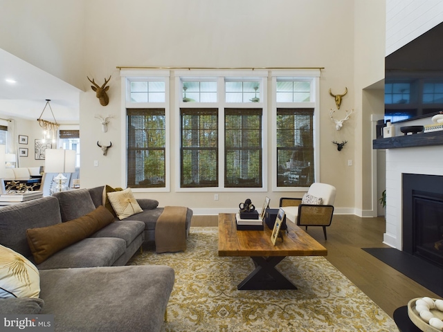 living room with a healthy amount of sunlight, a towering ceiling, an inviting chandelier, and hardwood / wood-style floors