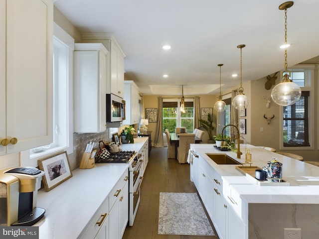 kitchen featuring white cabinets, a center island with sink, pendant lighting, high end white range, and sink