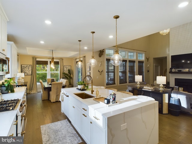 kitchen featuring an island with sink, hanging light fixtures, high end range, sink, and white cabinetry