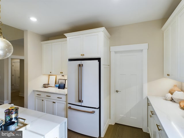 kitchen featuring dark wood-type flooring, hanging light fixtures, high end white fridge, and white cabinets