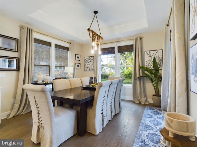 dining space with dark wood-type flooring, an inviting chandelier, and a raised ceiling