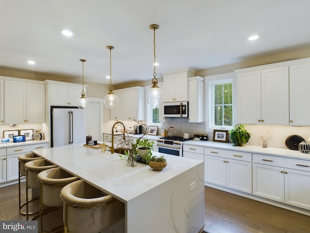 kitchen with high end appliances, a kitchen island with sink, white cabinetry, and dark hardwood / wood-style flooring