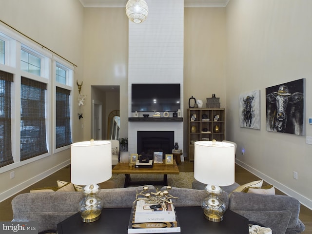 living room featuring a towering ceiling, crown molding, dark hardwood / wood-style floors, and a large fireplace