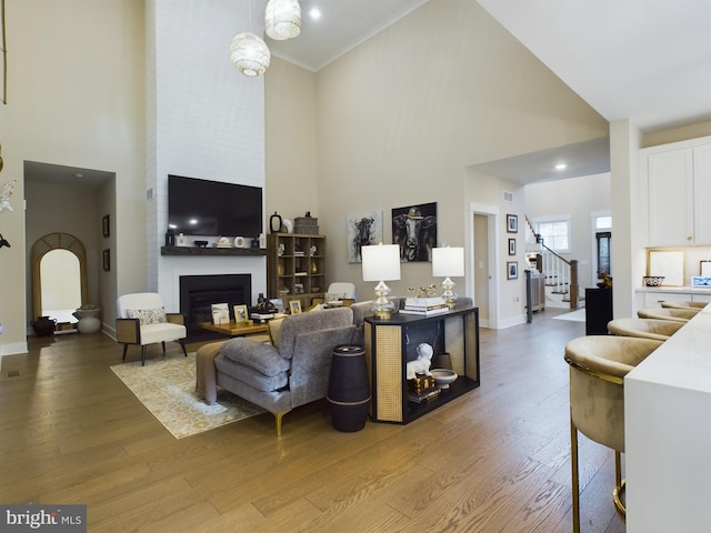 living room featuring crown molding, hardwood / wood-style floors, high vaulted ceiling, and a fireplace