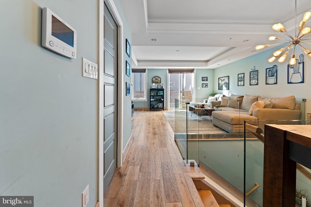 living room with an inviting chandelier, light wood-type flooring, and a raised ceiling