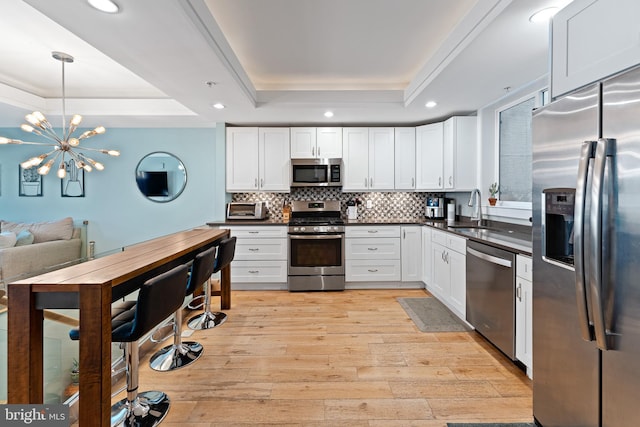 kitchen with appliances with stainless steel finishes, a tray ceiling, light wood-type flooring, and white cabinets