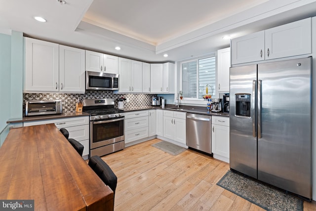 kitchen with white cabinets, appliances with stainless steel finishes, sink, wooden counters, and light hardwood / wood-style flooring