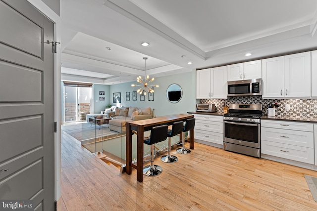 kitchen featuring appliances with stainless steel finishes, backsplash, a tray ceiling, light hardwood / wood-style floors, and white cabinets