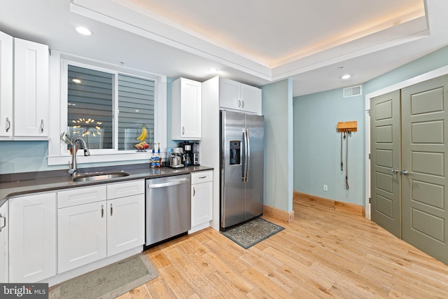 kitchen featuring appliances with stainless steel finishes, white cabinetry, a tray ceiling, light wood-type flooring, and sink