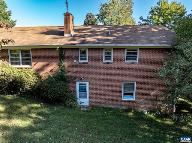 view of home's exterior featuring roof with shingles, a yard, brick siding, and a chimney
