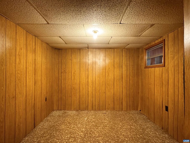 basement featuring wooden walls, a drop ceiling, and carpet floors