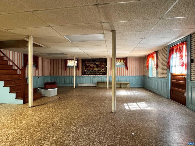 below grade area featuring wainscoting, a decorative wall, a drop ceiling, and stairs