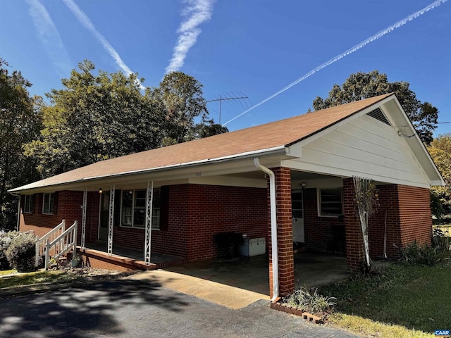 view of side of home with an attached carport, aphalt driveway, brick siding, and covered porch