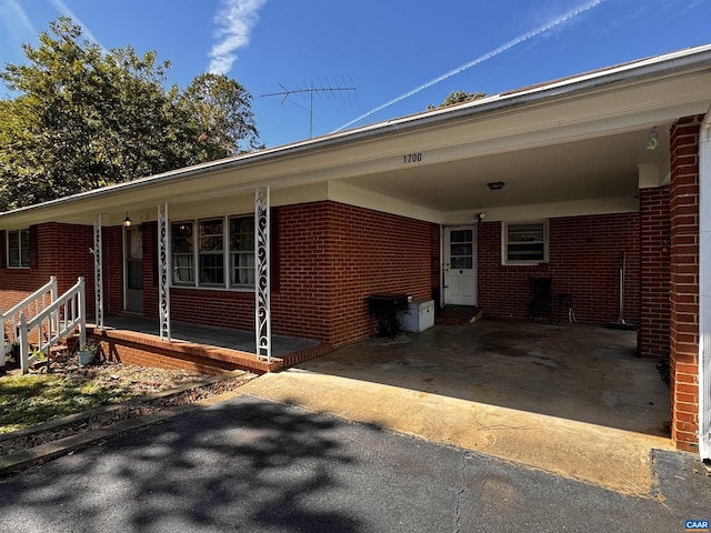 exterior space featuring an attached carport, a porch, brick siding, and driveway