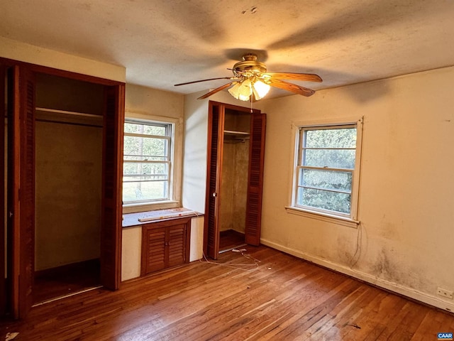 unfurnished bedroom with hardwood / wood-style floors, ceiling fan, baseboards, and multiple closets