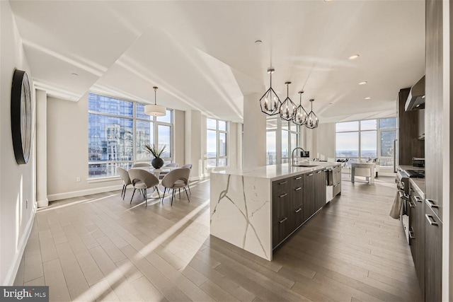 kitchen with wood-type flooring, wall chimney range hood, sink, a spacious island, and pendant lighting