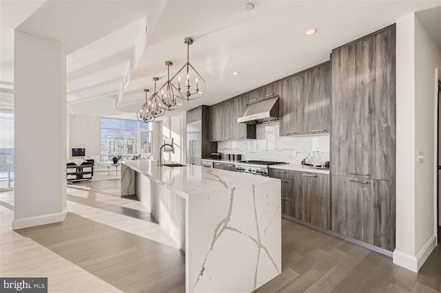 kitchen with light stone countertops, light hardwood / wood-style flooring, an island with sink, and decorative light fixtures