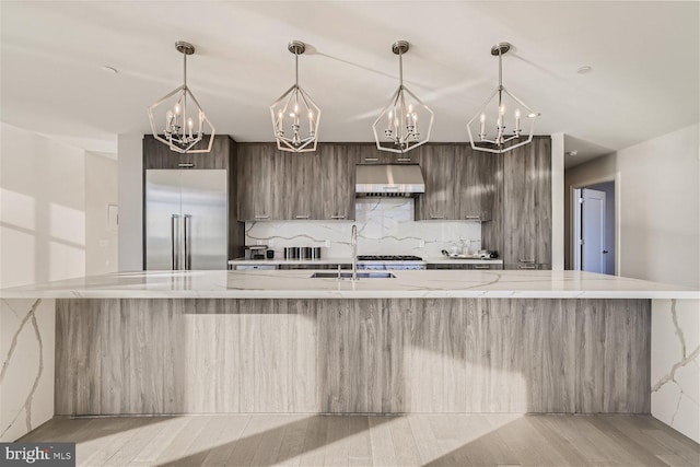 kitchen with a large island with sink, light stone countertops, built in fridge, light hardwood / wood-style floors, and sink