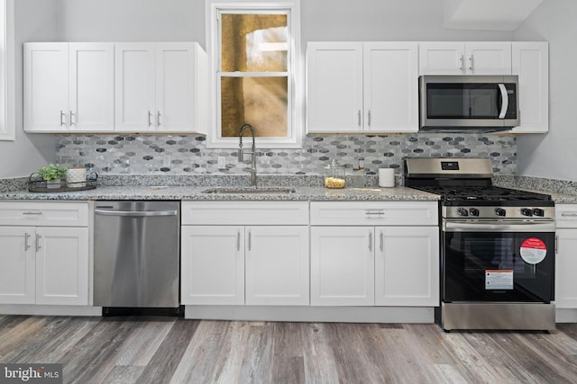 kitchen with appliances with stainless steel finishes, white cabinetry, sink, and light wood-type flooring