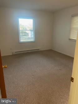 unfurnished room featuring a baseboard heating unit and carpet flooring