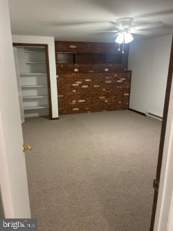 interior space featuring ceiling fan, brick wall, carpet floors, and a baseboard heating unit