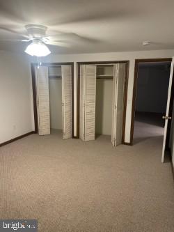 unfurnished bedroom featuring multiple closets, light colored carpet, and ceiling fan