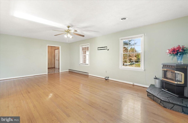 unfurnished living room with light hardwood / wood-style floors, a wood stove, a baseboard heating unit, and ceiling fan