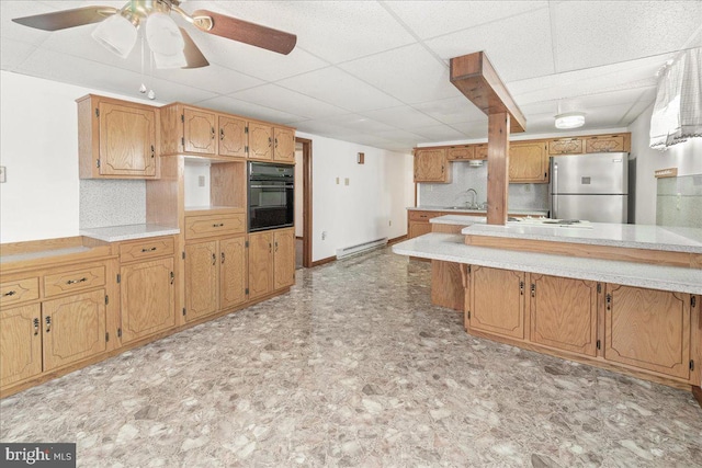 kitchen featuring a drop ceiling, a baseboard heating unit, ceiling fan, black oven, and stainless steel refrigerator