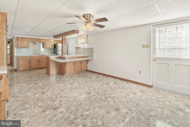 kitchen featuring a drop ceiling, kitchen peninsula, stainless steel fridge, and sink